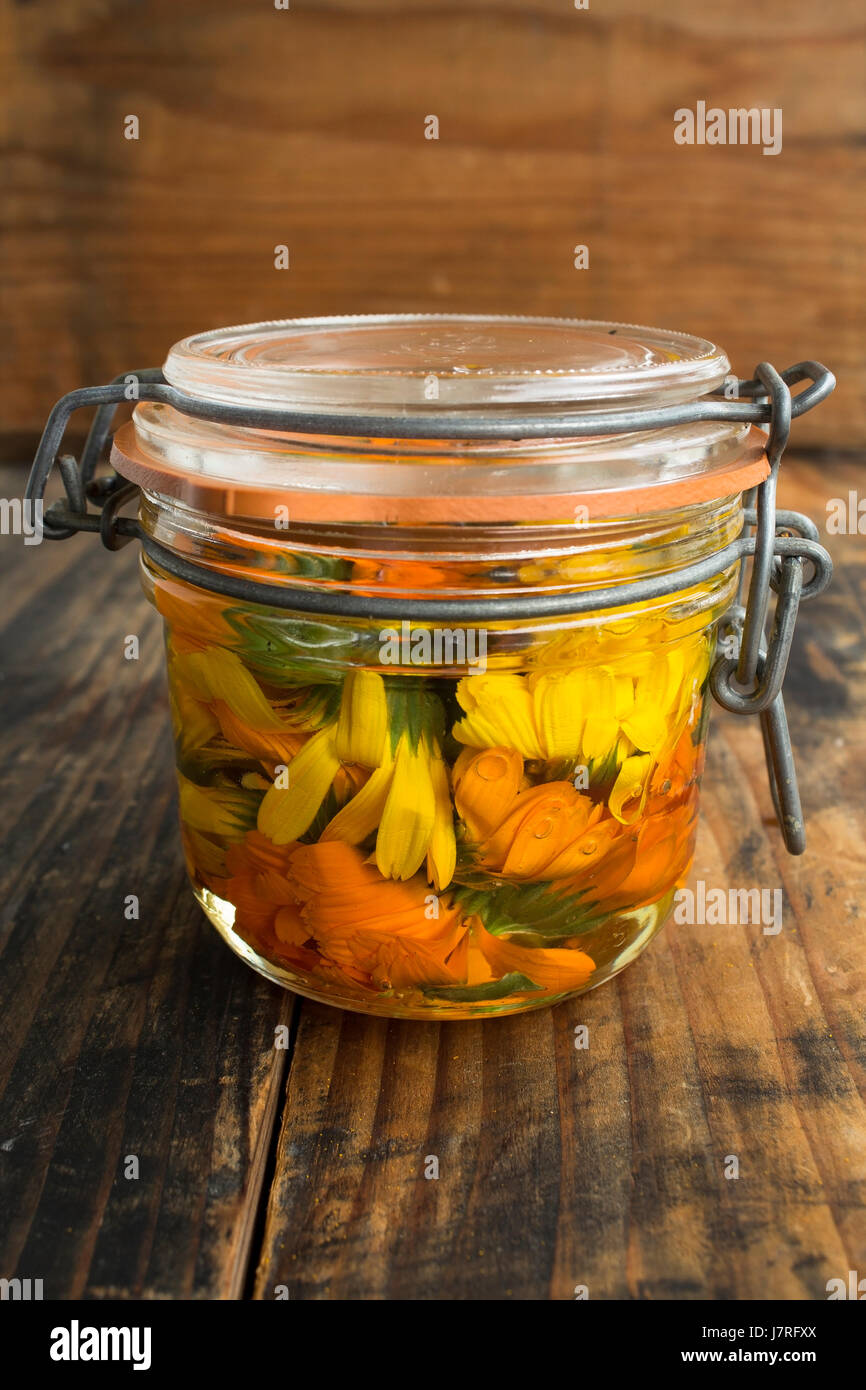 Calendula-Öl in einem Glas auf einem rustikalen hölzernen Hintergrund. Stockfoto