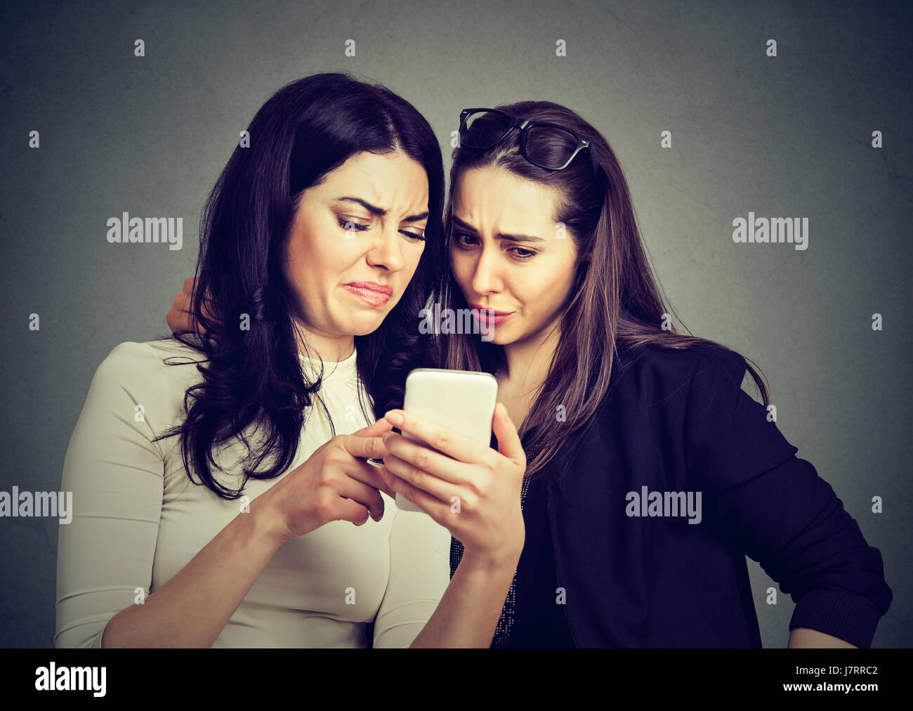 Zwei Freunde Frauen anzeigen auf Linie Inhalt auf einem Smartphone auf grauem Hintergrund isoliert verärgert Stockfoto