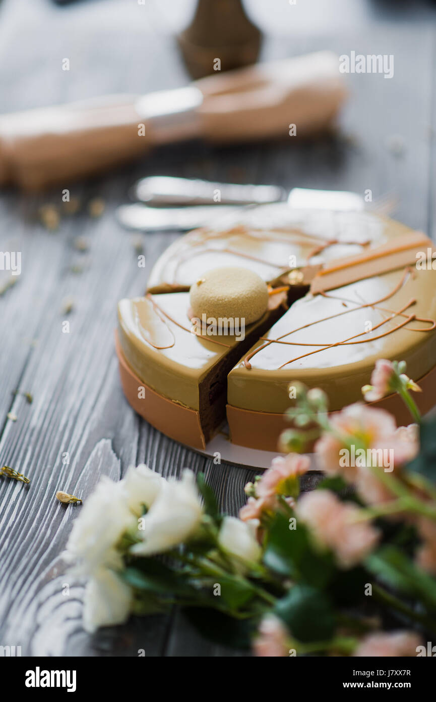 Bäckerei mit ungewöhnlich gelbe Mousse Torte mit Mandel-Dacquoise, Himbeer-Confit, knusprige Schicht mit karamellisierten Haselnüssen und Himbeere Pulver, Mousse, basierend auf Bitterschokolade serviert auf Holztisch Stockfoto