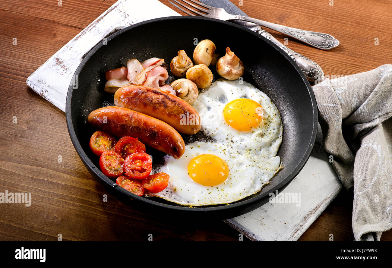 Englisches Frühstück mit Eiern, Würstchen, Speck, Bohnen und Champignons in Pfanne Stockfoto