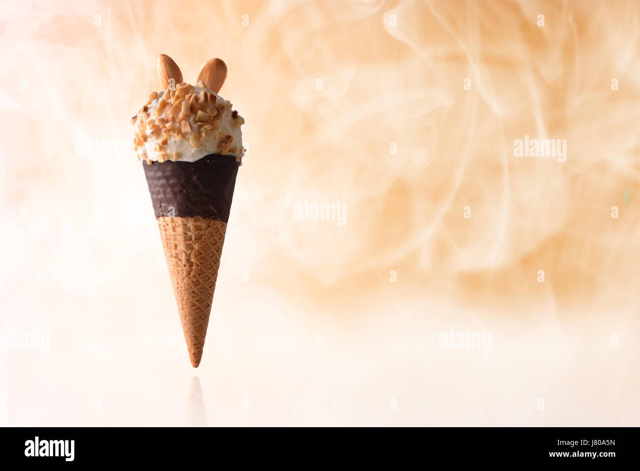 Ice Cream cone aromatisierte Sahne Mandel. Erhöhten auf reflektierenden Tisch und garniert mit kleinen Stücken von Mandeln. Mit orangem Hintergrund und kaltem Dampf. H Stockfoto