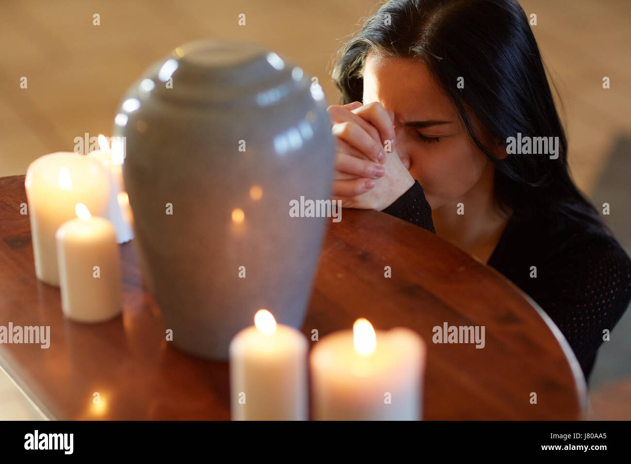 traurige Frau mit Grabbeigaben Urn beten in der Kirche Stockfoto