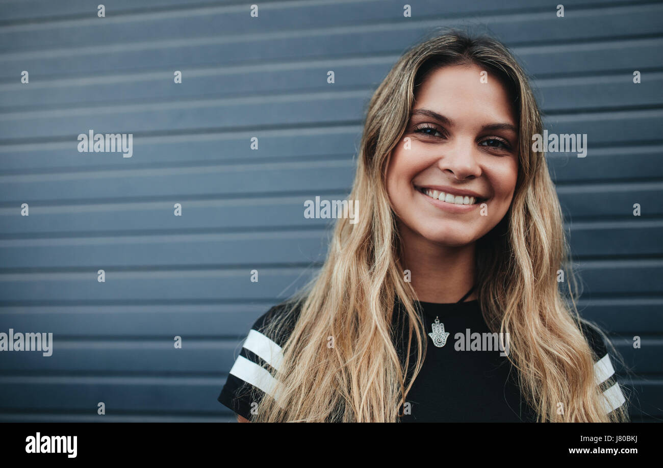 Porträt von lächelnden jungen weiblichen stehend gegen graue Wand hautnah. Schöne kaukasischen junge Frau Blick in die Kamera und lächelnd. Stockfoto