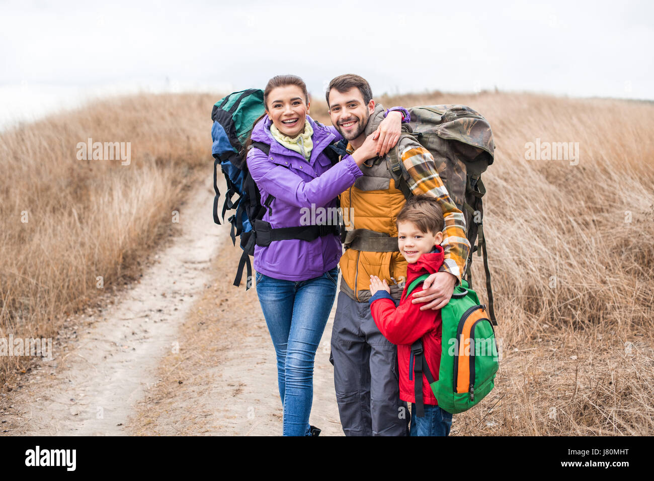 Glückliche Familie mit Rucksäcken auf ländlichen Weg am trüben Herbsttag umarmt Stockfoto
