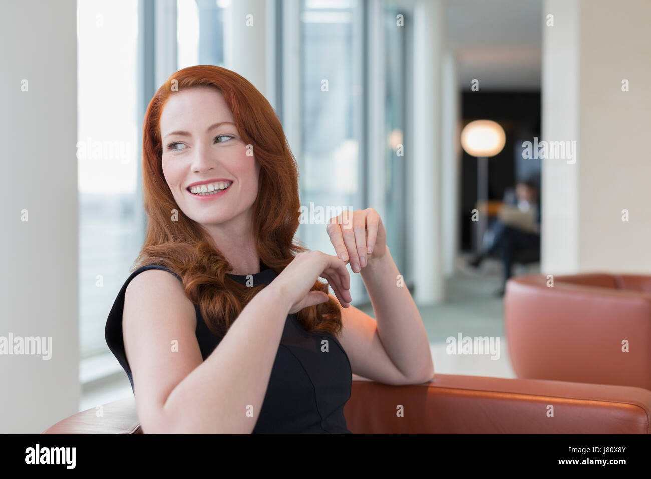 Lächelnd Geschäftsfrau mit roten Haaren, die auf der Suche über die Schulter in lounge Stockfoto