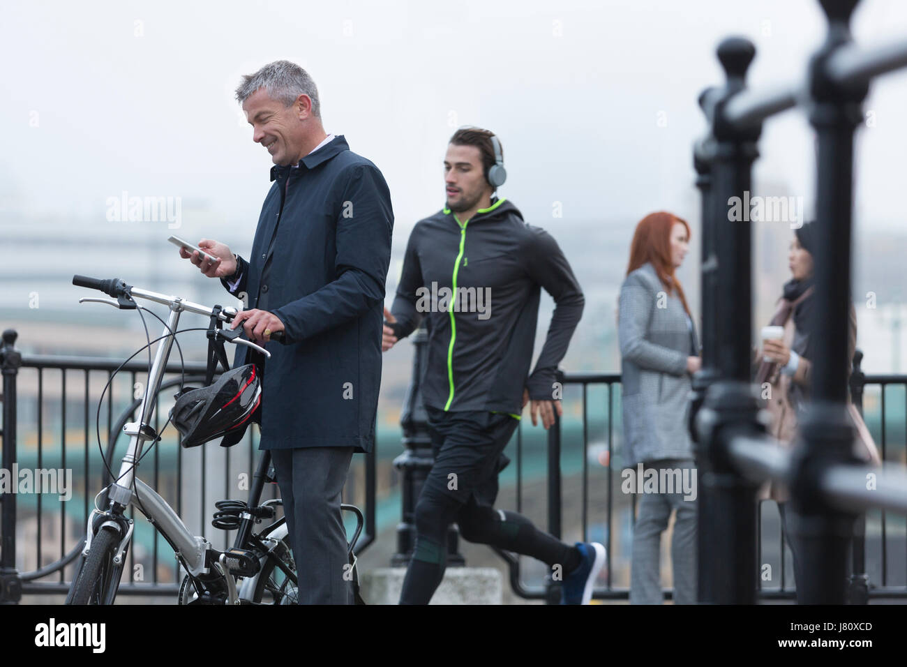 Geschäftsmann mit Fahrrad SMS mit Handy und männliche Läufer auf städtischen Rampe Stockfoto