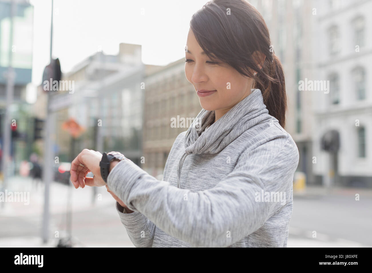Lächelnde weibliche Läufer Check-Armbanduhr auf städtischen Bürgersteig Stockfoto