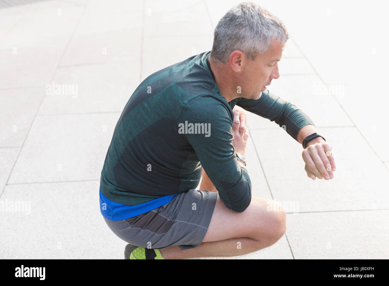 Männliche Läufer ausruhen, hocken und Überprüfung Armbanduhr Stockfoto