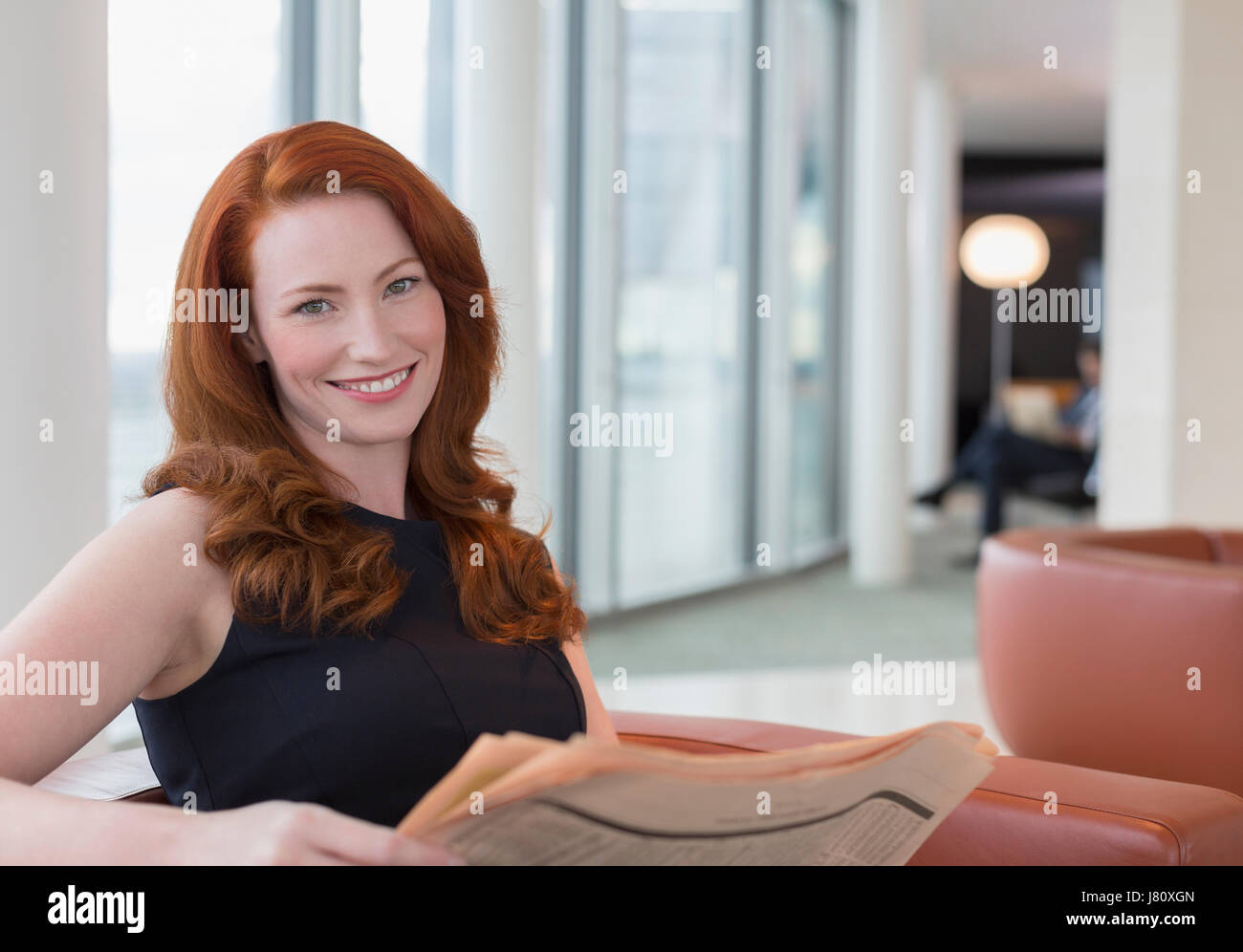 Porträt lächelnd Geschäftsfrau mit roten Haaren Zeitunglesen im Büro lounge Stockfoto