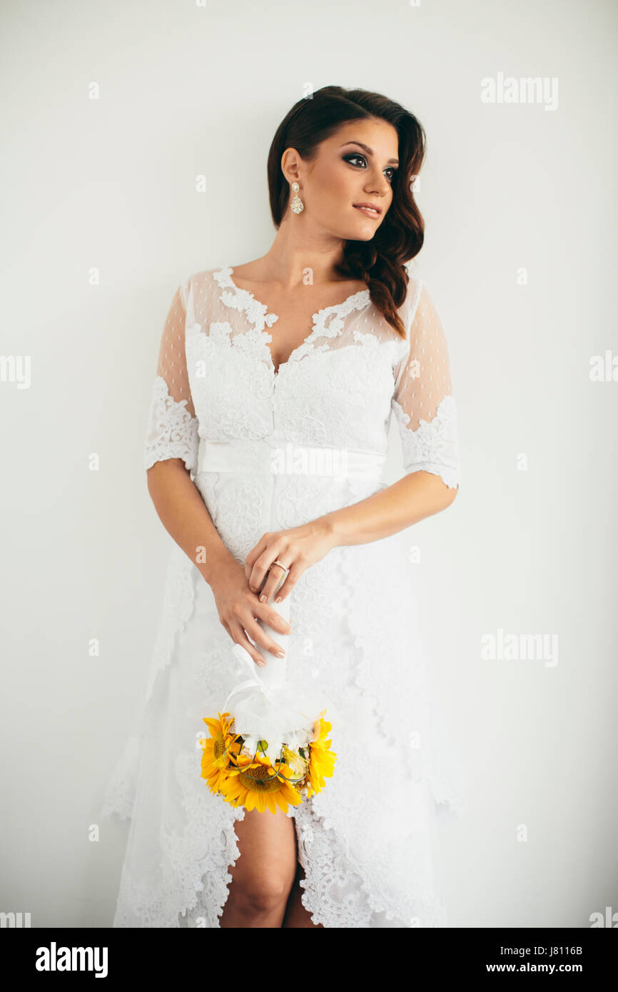 Schöne junge Braut posiert in einem Hochzeitskleid und halten einen Strauß Sonnenblumen Stockfoto