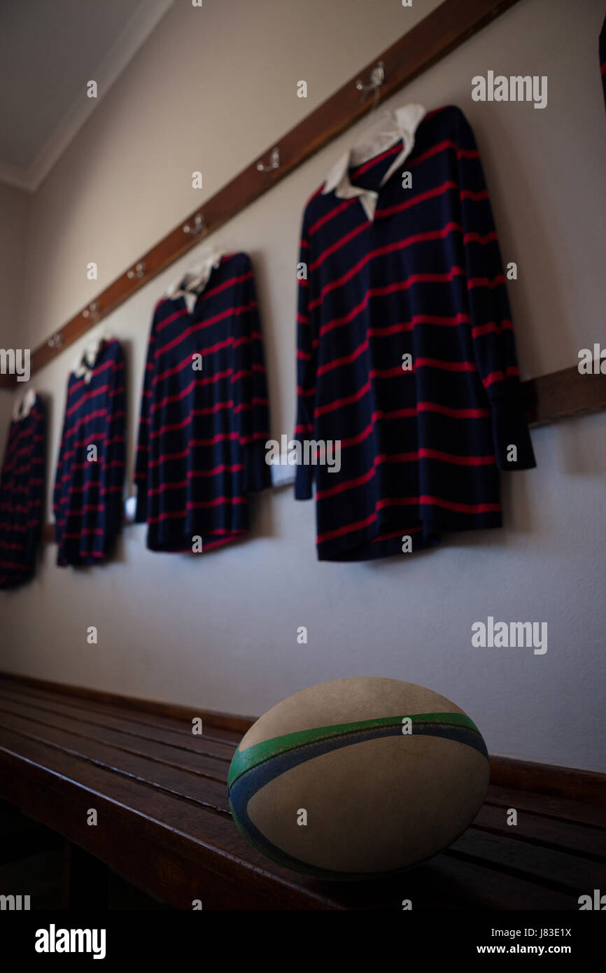 Rugby-Ball auf Bank gegen gestreifte T-shirts hängen in Umkleidekabine Stockfoto