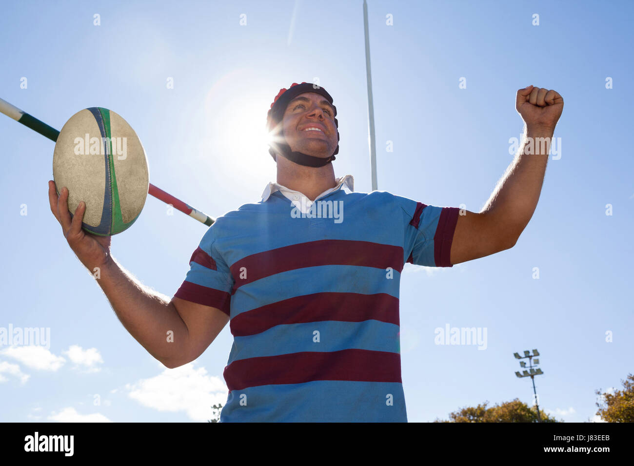 Niedrigen Winkel Ansicht der glückliche Spieler mit Rugby-Ball mit Ziel auf dem Postweg gegen blauen Himmel erhobenen Armen Stockfoto