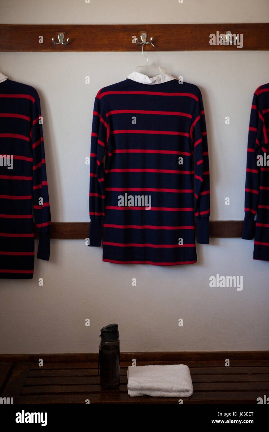 Flasche und Serviette auf Bank gegen Rugby-Shirts hängen in Umkleidekabine Stockfoto