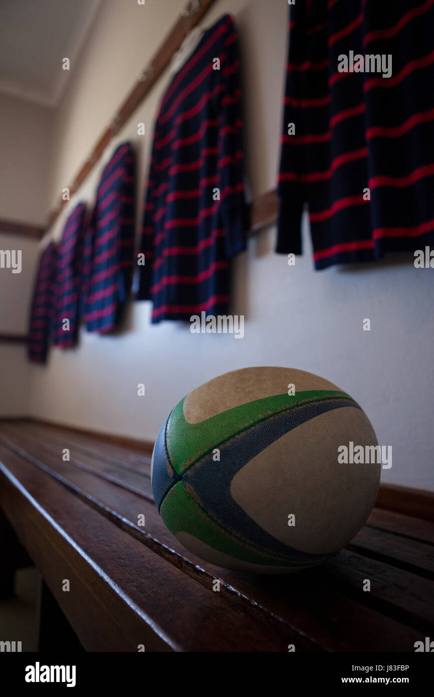 Rugby-Ball auf Bank gegen T-shirts hängen in Umkleidekabine Stockfoto