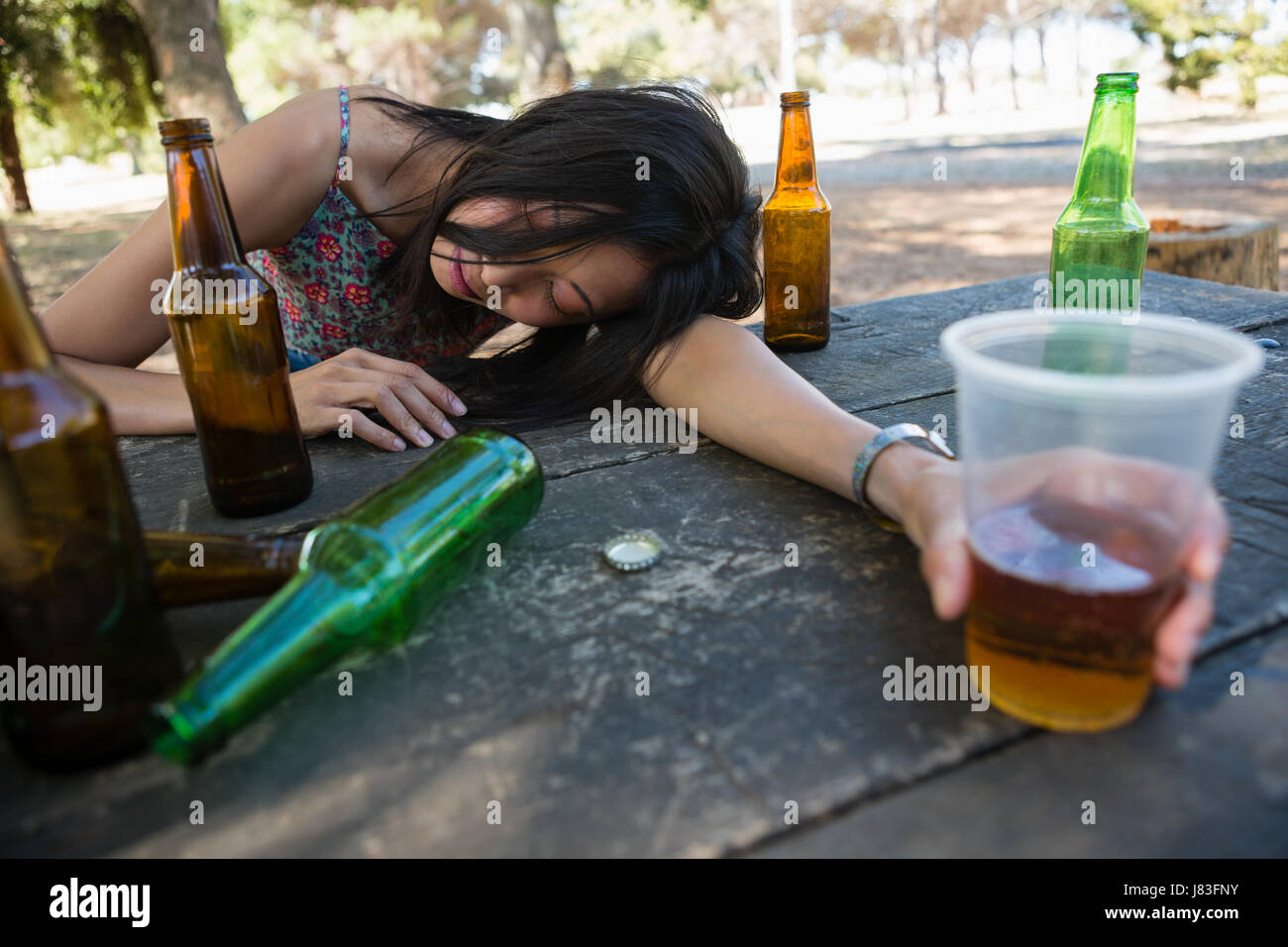 Betrunkene Frau entspannend auf dem Tisch mit einem Glas im park ...