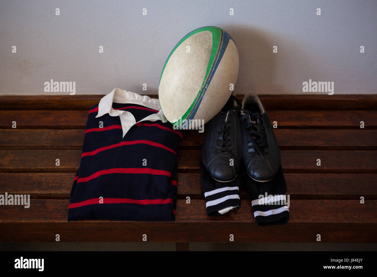 Erhöhte Ansicht des Rugby-Ball und Kleidung mit Schuhen auf Bank in Umkleidekabine Stockfoto