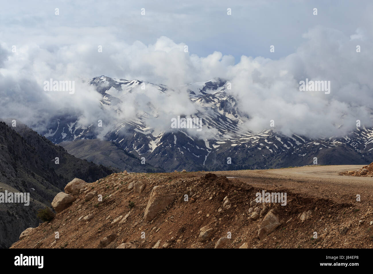 Horizontale schuss Berglandschaft mit Serpentinenstraße auf Vorder- und verschwommen Gipfel mit Schnee bedeckt mit Wolken im Hintergrund Stockfoto