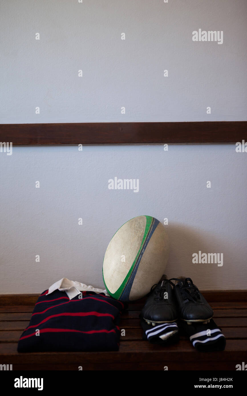 Rugby-Ball mit Kleidung und Schuhe auf Bank gegen die Wand Stockfoto
