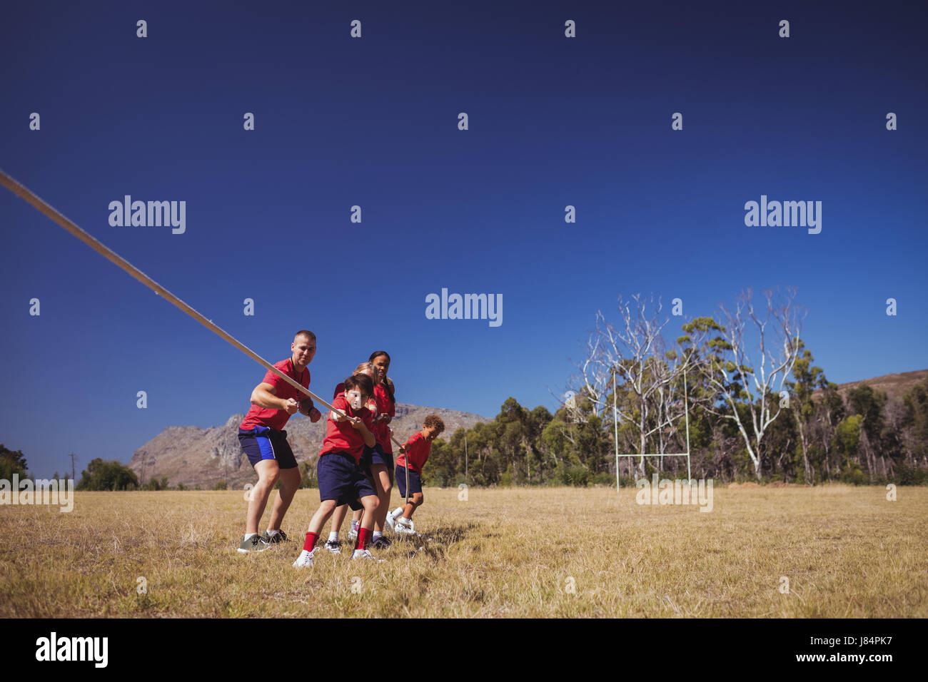 Trainer unterstützen Kinder im Tauziehen beim Hindernis-Parcours-Training im Boot camp Stockfoto