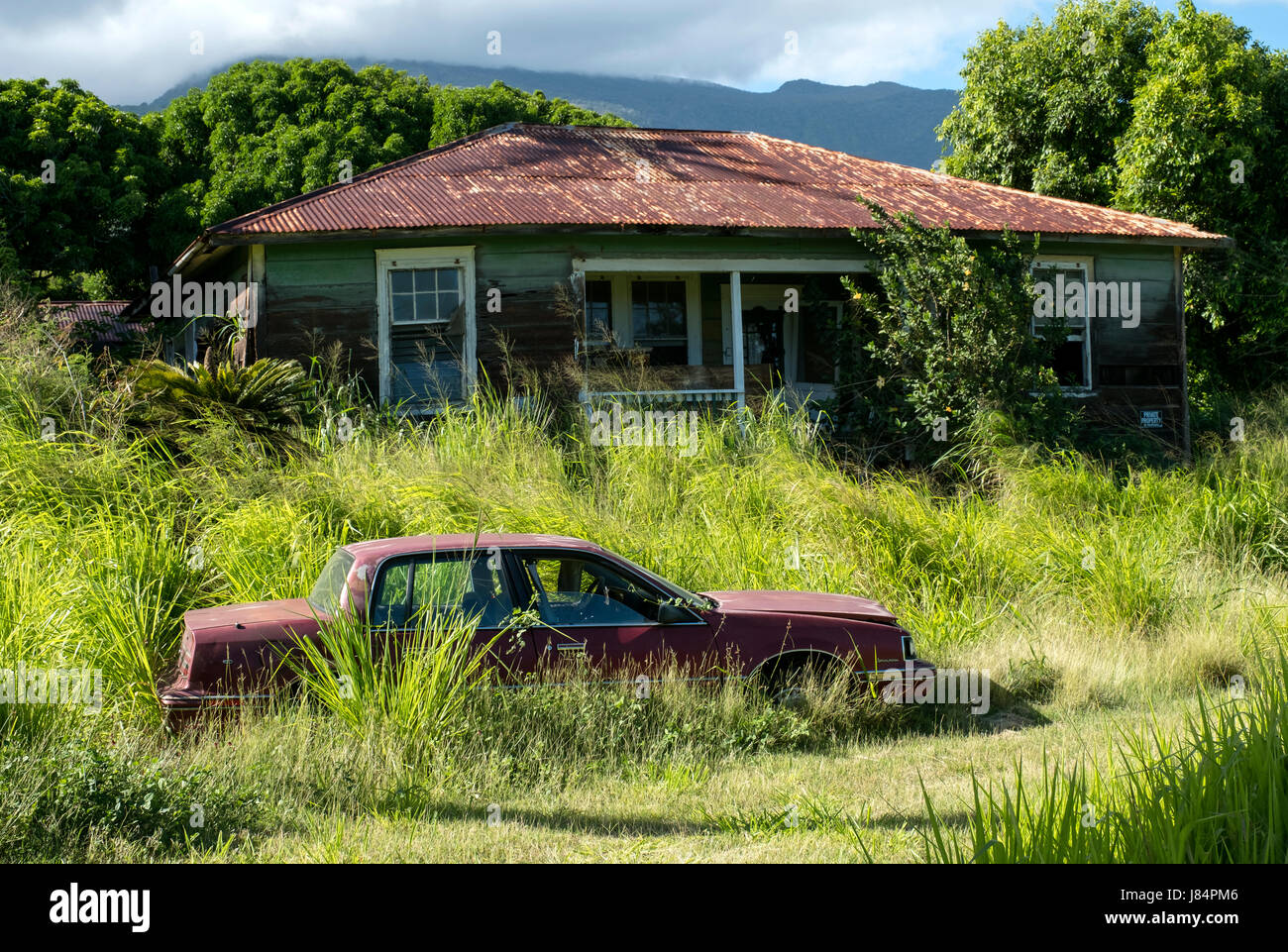 ein verlassenes Auto sitzt in einem Hof neben einer verfallenen Eigenschaft der Pi'ilani-Autobahn im Süden Maui, Hawaii Stockfoto