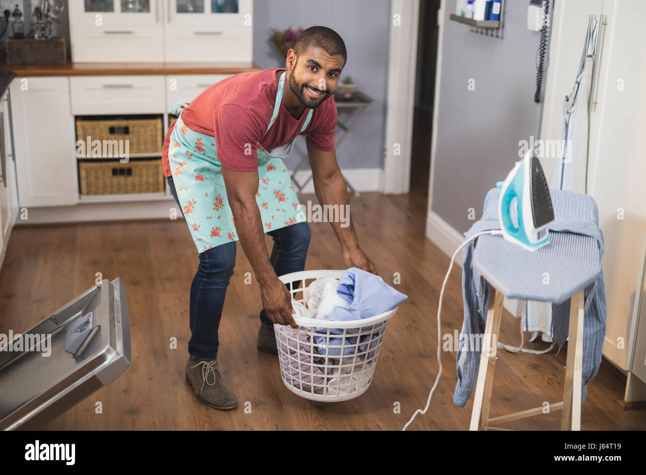 Porträt des lächelnden jungen Mannes anheben Wäschekorb Bügelbrett in Küche zu Hause Stockfoto