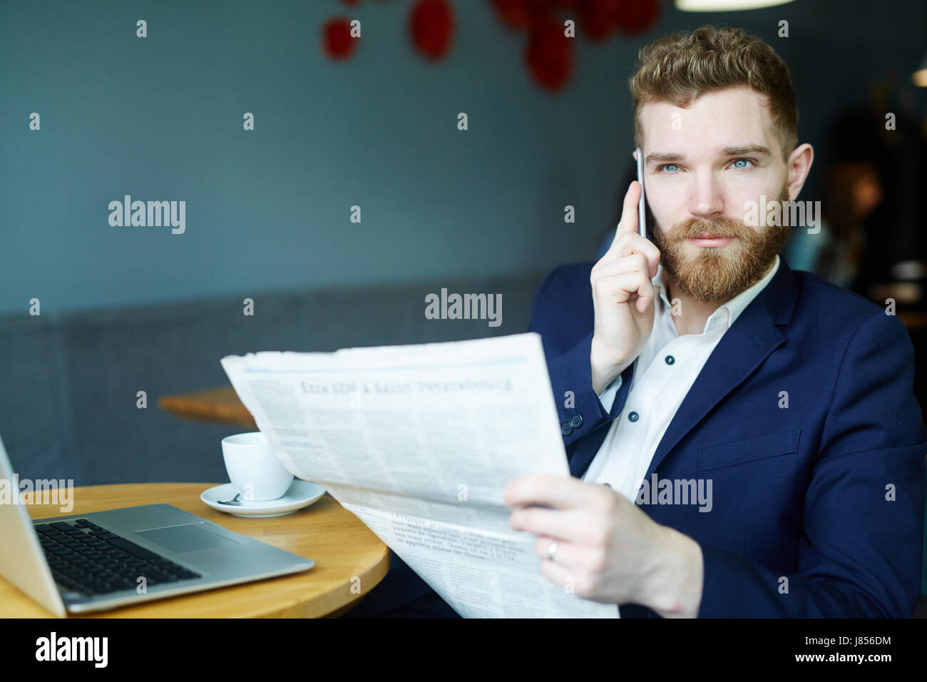 Porträt von hübscher junger Geschäftsmann sprechen per Smartphone beim lesen Zeitung im café Stockfoto