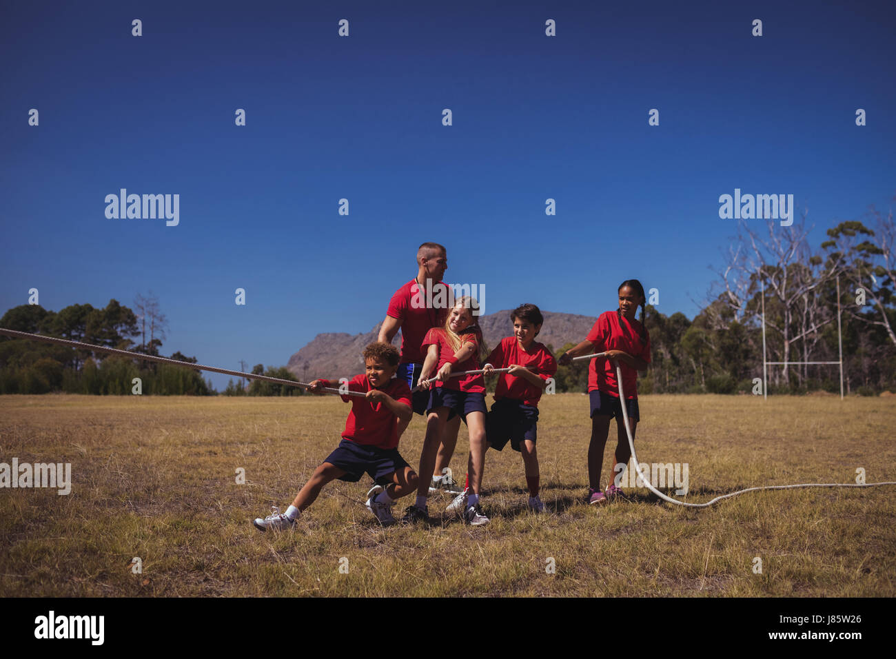 Trainer unterstützen Kinder im Tauziehen beim Hindernis-Parcours-Training im Boot camp Stockfoto