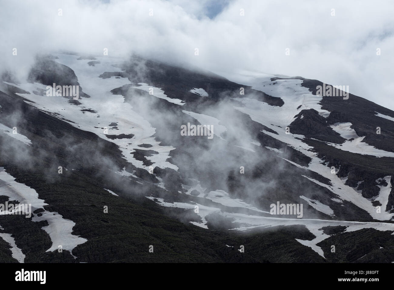 Horizontale Schuß von Berghängen durch schmelzenden Schnee und Wolken bedeckt Stockfoto