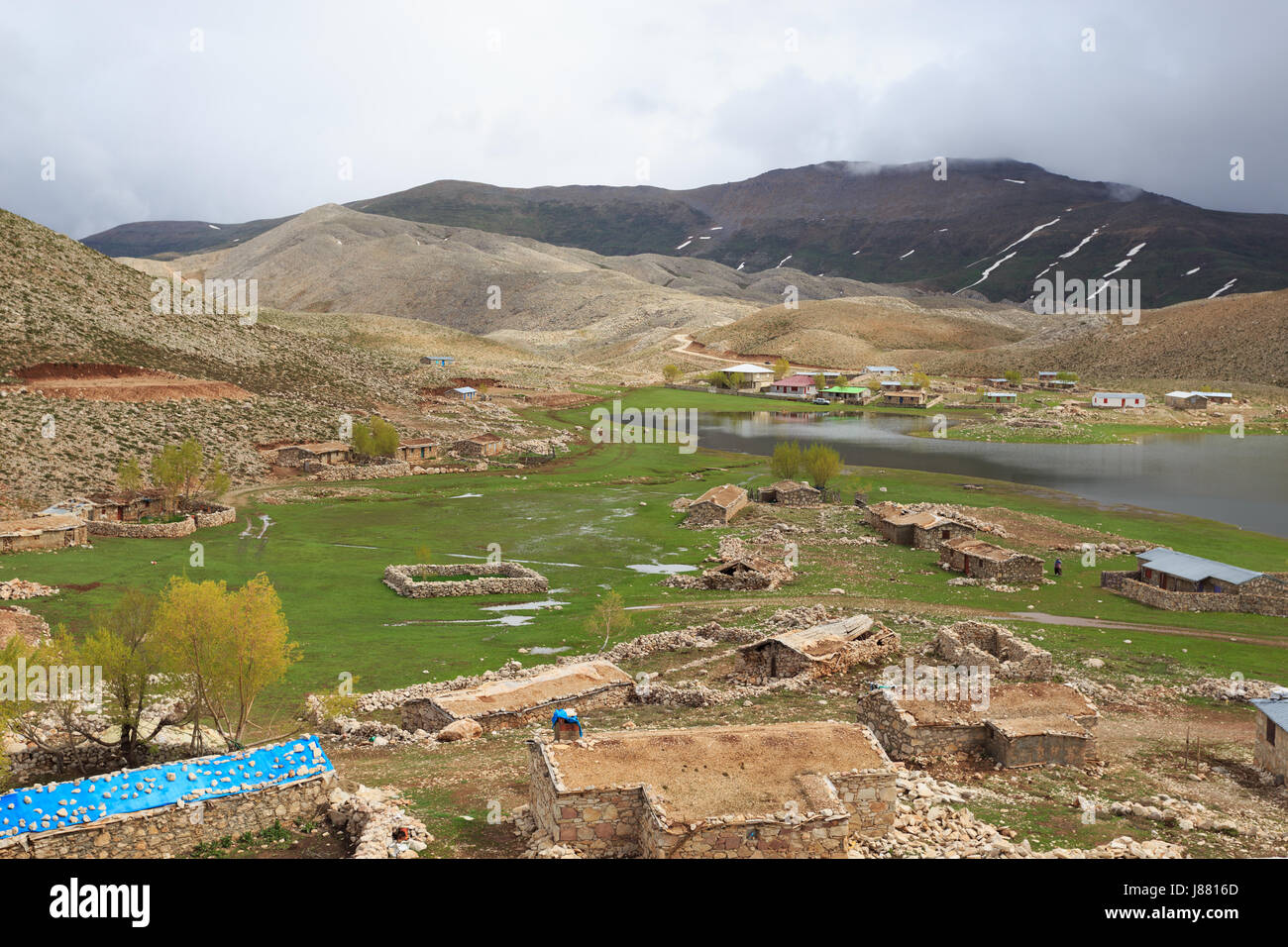 Horizontalen Schuss Berglandschaft mit hängen vom schmelzenden Schnee Bergsee und kleine Steinhäuser Stockfoto