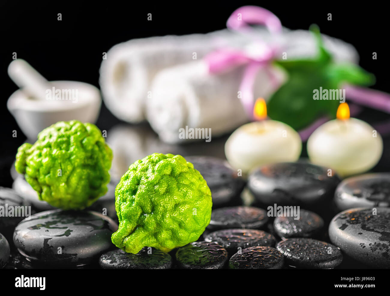 Spa-Konzept von Bergamotte Obst, Blatt, Kerzen, Mörtel, weiße Handtücher und Zen Basaltsteinen mit Wassertropfen auf schwarzem Hintergrund Stockfoto
