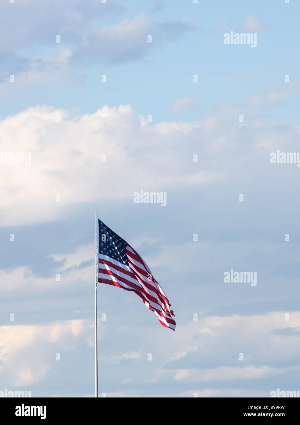 Vertikale amerikanische Flagge gegen einen hellblauen Himmel mit dünnen Wolken. Die Wolke ist im Wind entfaltet. Stockfoto