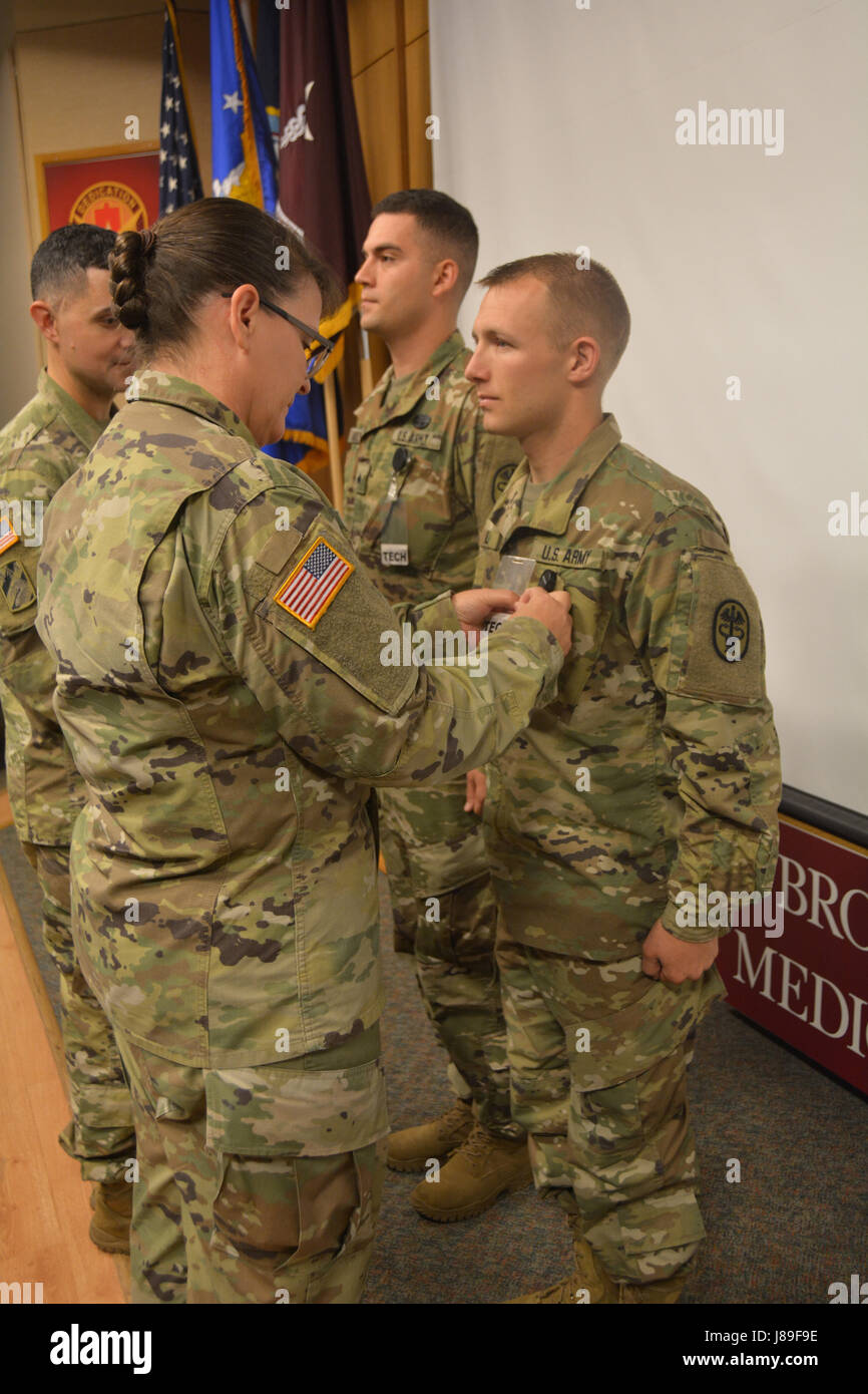 Armee Oberst Margaret Nava, chief Nursing Officer präsentiert Sgt. Matthew Reynolds und Spc. Tyler Hull, ihre silberne Ehrennadel als Bestandteil der 68W Auslastung Programm Mai 11 während der Krankenschwestern Woche Feier in der Aula Brooke Army Medical Center. Das silberne Abzeichen bedeutet, dass sie ihre Kompetenzen innerhalb einer Patientenversorgung Einstellung erzielt haben. (US Armee-Foto von Robert Schilde) Stockfoto