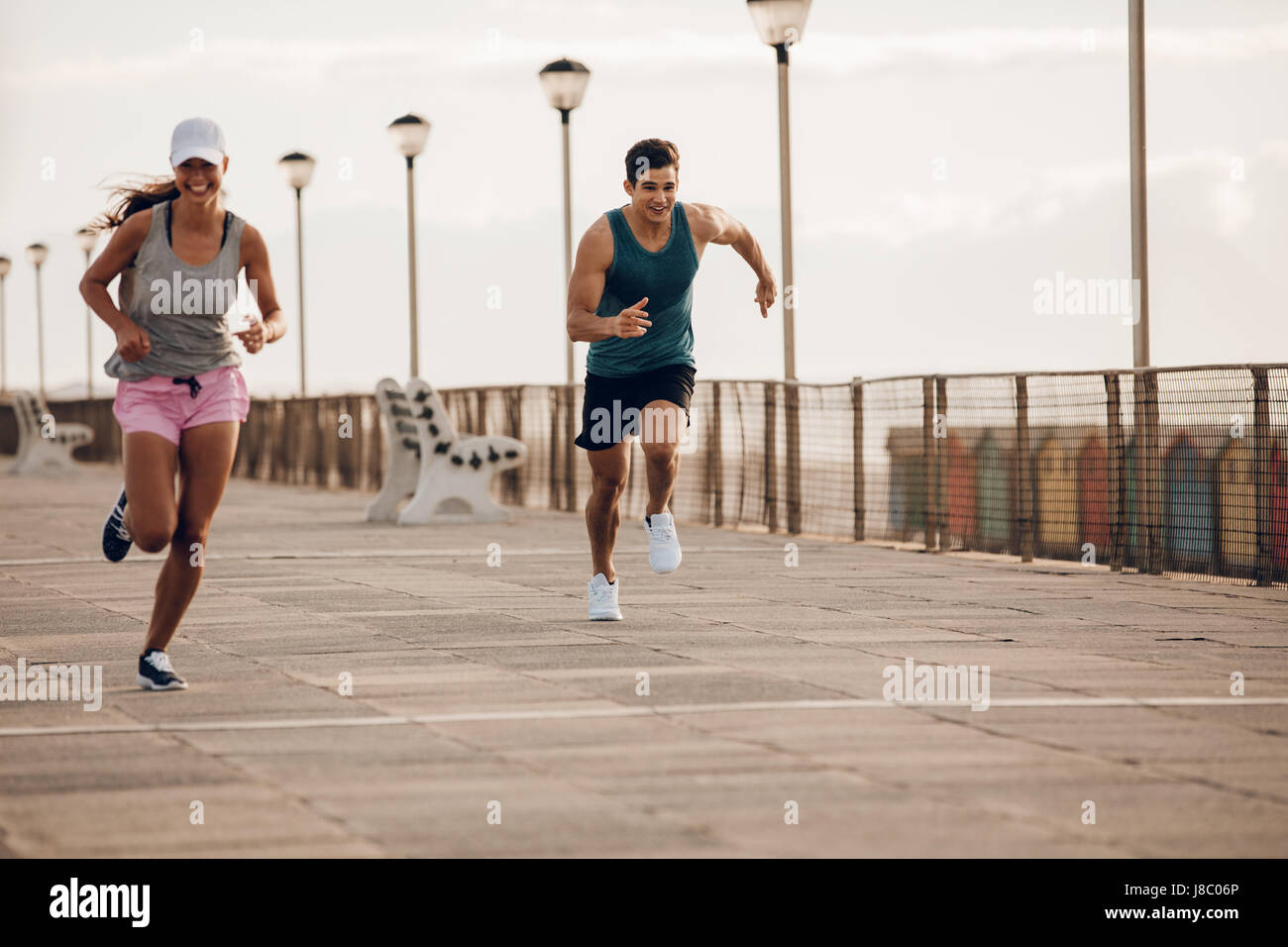 Zwei junge Menschen an einer Strandpromenade sprinten. Passen Sie die jungen Läufer gemeinsam an einer Straße am Meer. Stockfoto