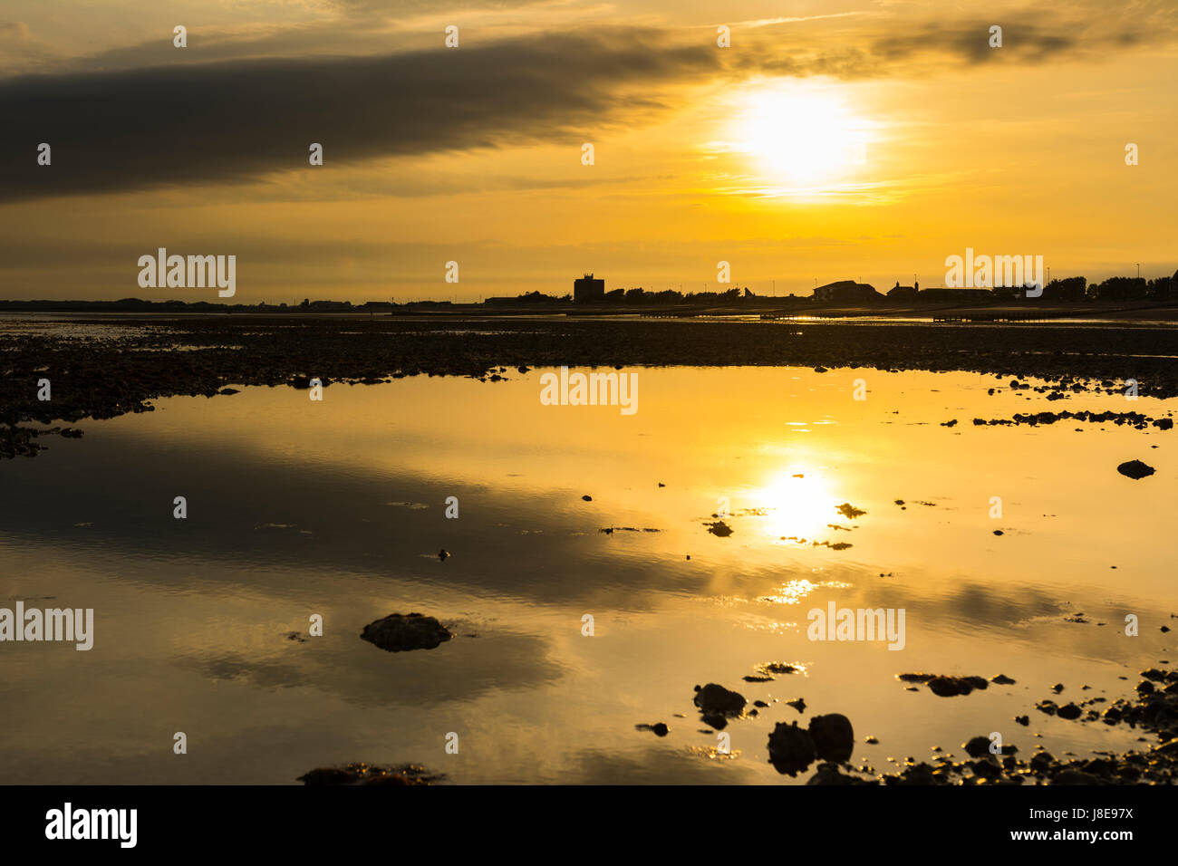 Reflexionen einer niedrigen Sonne im verbleibenden Wasser bei Ebbe an einem Strand in Großbritannien. Stockfoto