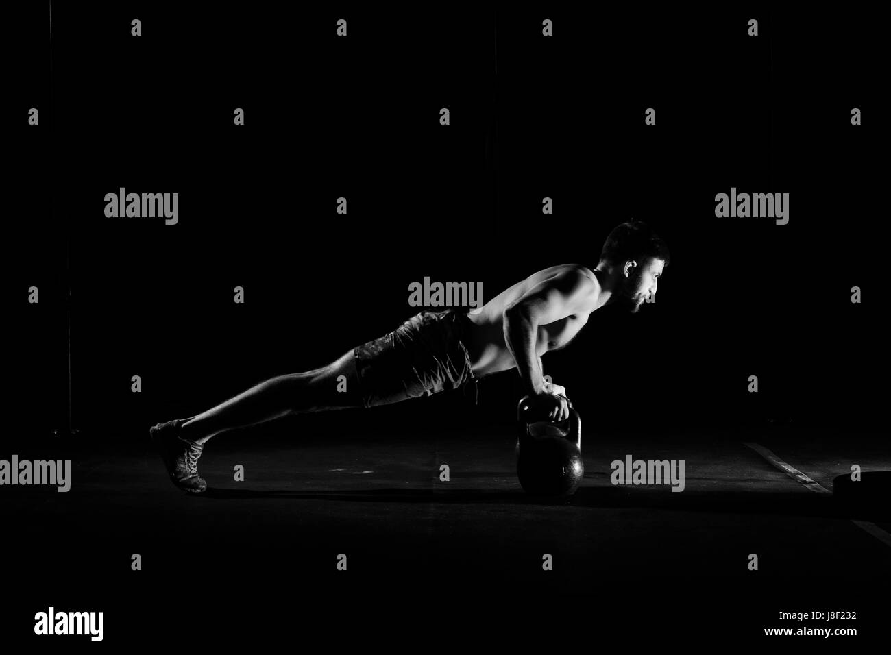Fitness-Training. Mann tut Push ups Übung mit Hanteln oder Gewichte in dunklen Turnhalle. Stockfoto