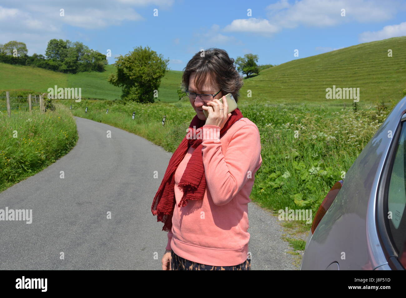 Frau stehend mit dem Briefpapier Auto auf einen Feldweg, Handy Hilfe anfordern Stockfoto