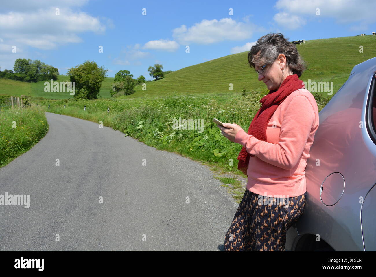 Frau stehend mit dem Briefpapier Auto auf einen Feldweg, Handy Hilfe anfordern Stockfoto