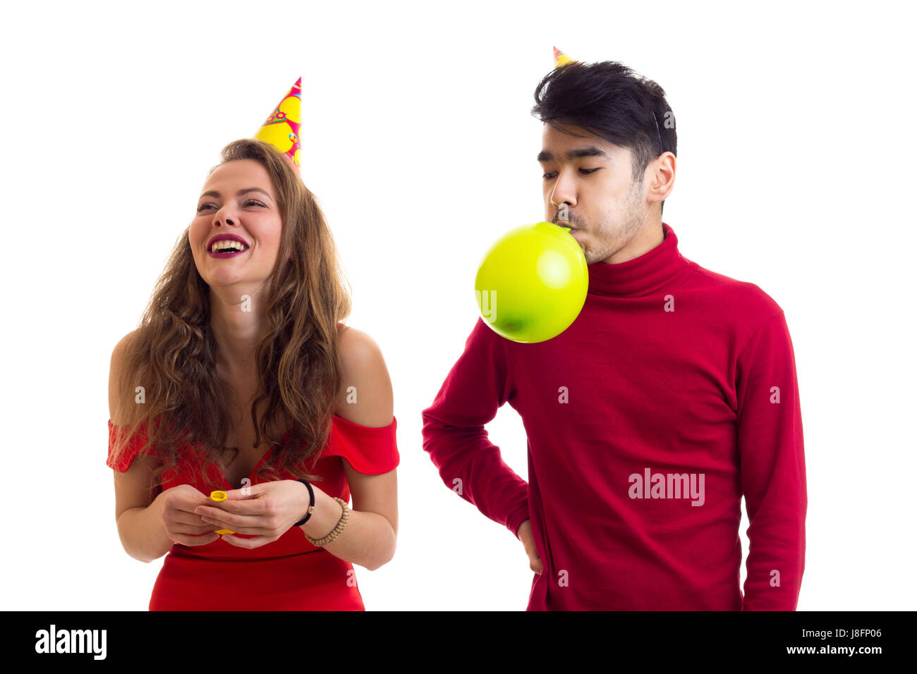 Junge glücklich Frau mit lange kastanienbraunes Haar im roten Kleid mit farbigen Hut und schönen jungen Mann im roten Hemd bläst Luftballons auf weißem Hintergrund in St. Stockfoto