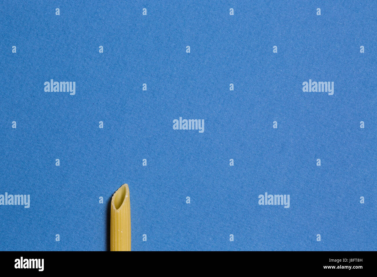 Einzelne Pasta Penne Rohr auf blauem Hintergrund. Abstrakte konzeptuelle Foto mit Textfreiraum. Stockfoto