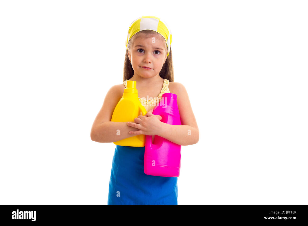 Lustige kleine Mädchen mit langen kastanienbraunes Haar in gelbes Hemd und blaue Schürze mit gelbem Kopftuch halten gelbe und rosa Flaschen auf weißem Hintergrund in s Stockfoto