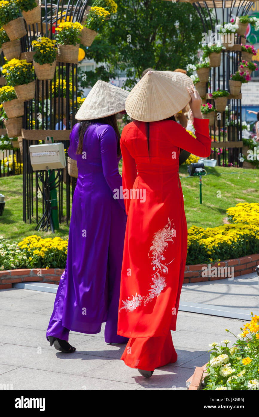 Ho-Chi-Minh-Stadt, Vietnam - 7. Februar 2016: Zwei junge vietnamesische Frauen in Tracht Ao Dai für Bilder vorne Blumenbeete zu posieren Stockfoto