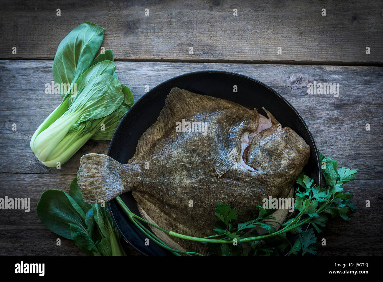 Ein Steinbutt, umgeben von jungem Gemüse; Essen; Fisch; Meeresfrüchte; Plattfische; Zutaten für eine Mahlzeit; Ungekocht; RAW; Gesunde Ernährung; Fischgericht Stockfoto