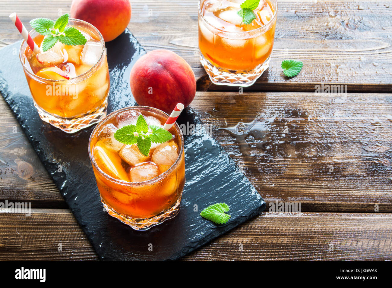 Pfirsich Eistee. Eistee mit Pfirsich Scheiben, Minze und Eiswürfel auf Schiefer und Holz rustikal Hintergrund hautnah. Hausgemachte erfrischendes Sommergetränk. Stockfoto