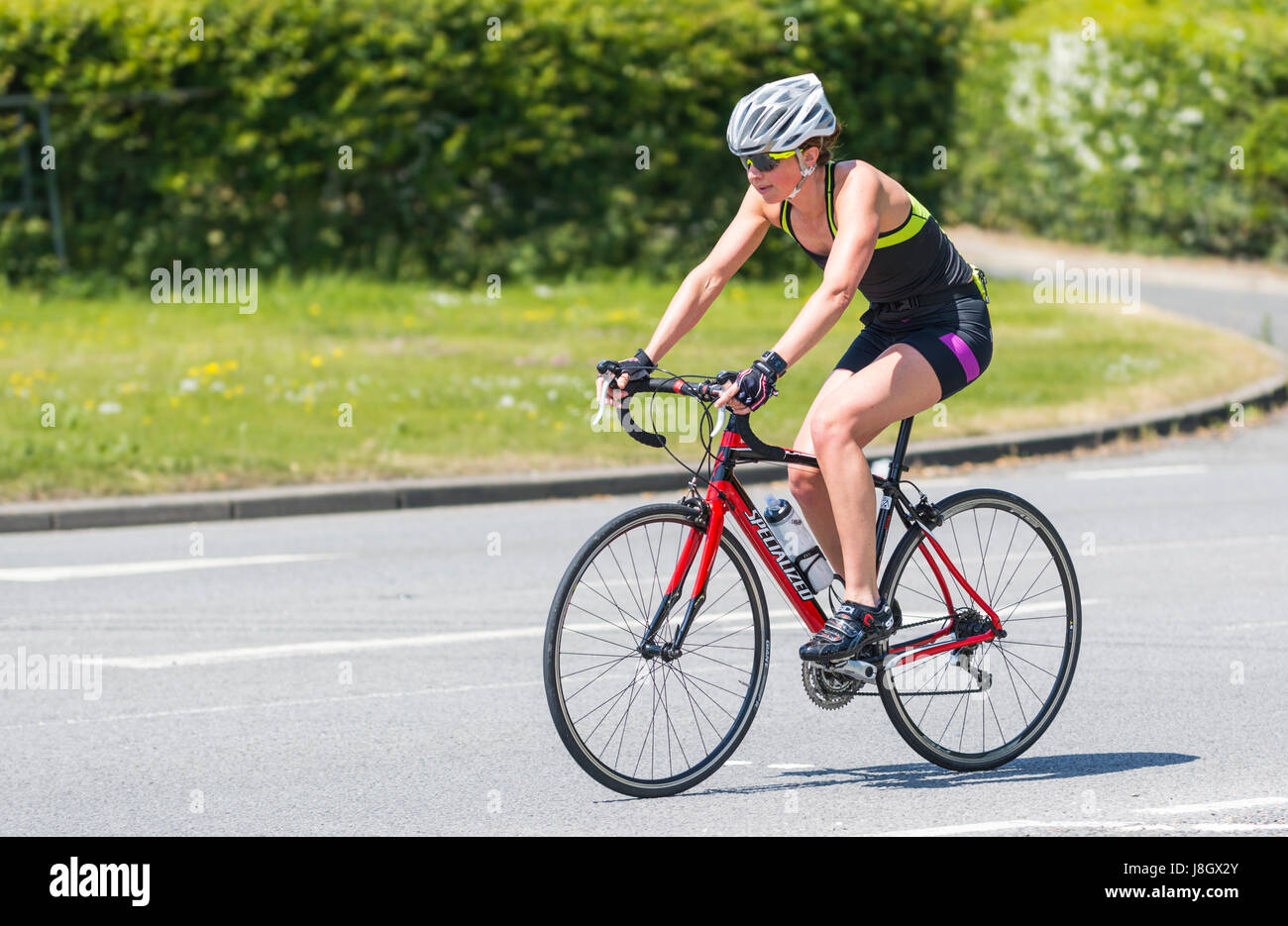 Frau auf einer Straße, die das Tragen eines Helmes an einem sonnigen Tag Radfahren. Stockfoto