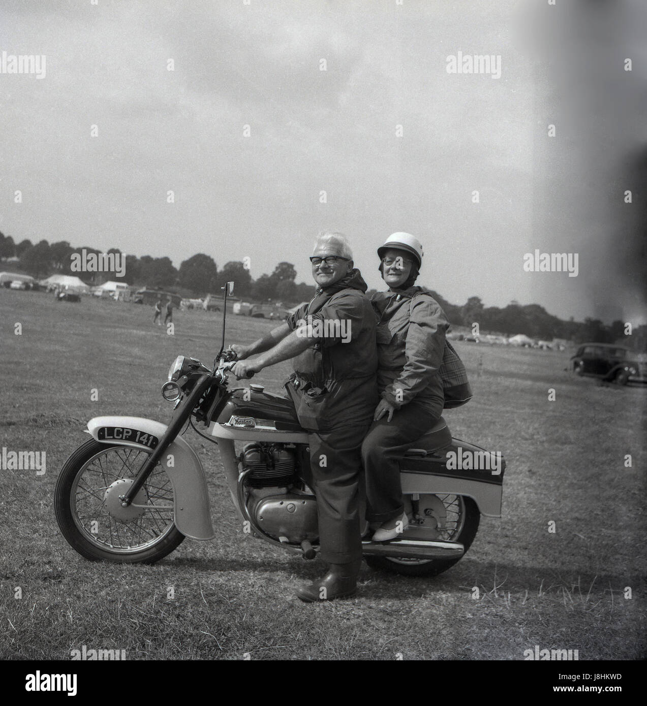 England, 1959, historisch, Motorradfahren, draußen auf einem Feld, ein glückliches älteres Paar auf ihrem britischen Norton Motorrad sitzend, mit der Frau auf dem Rücken als Sozius. Stockfoto