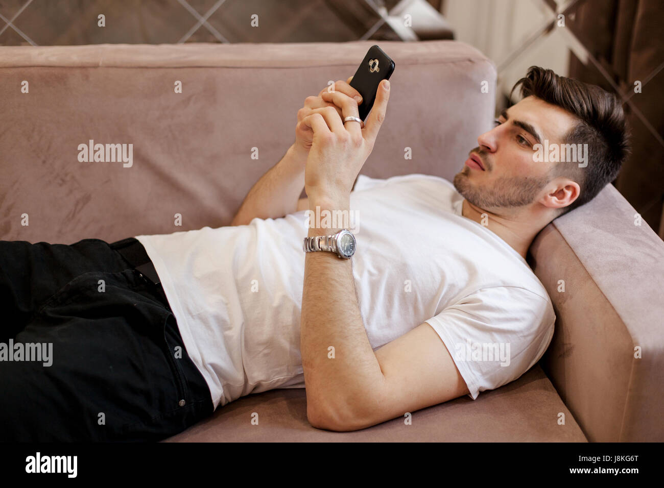 Gut aussehender Mann mit Smartphone zu Hause auf der Couch liegend. Stockfoto