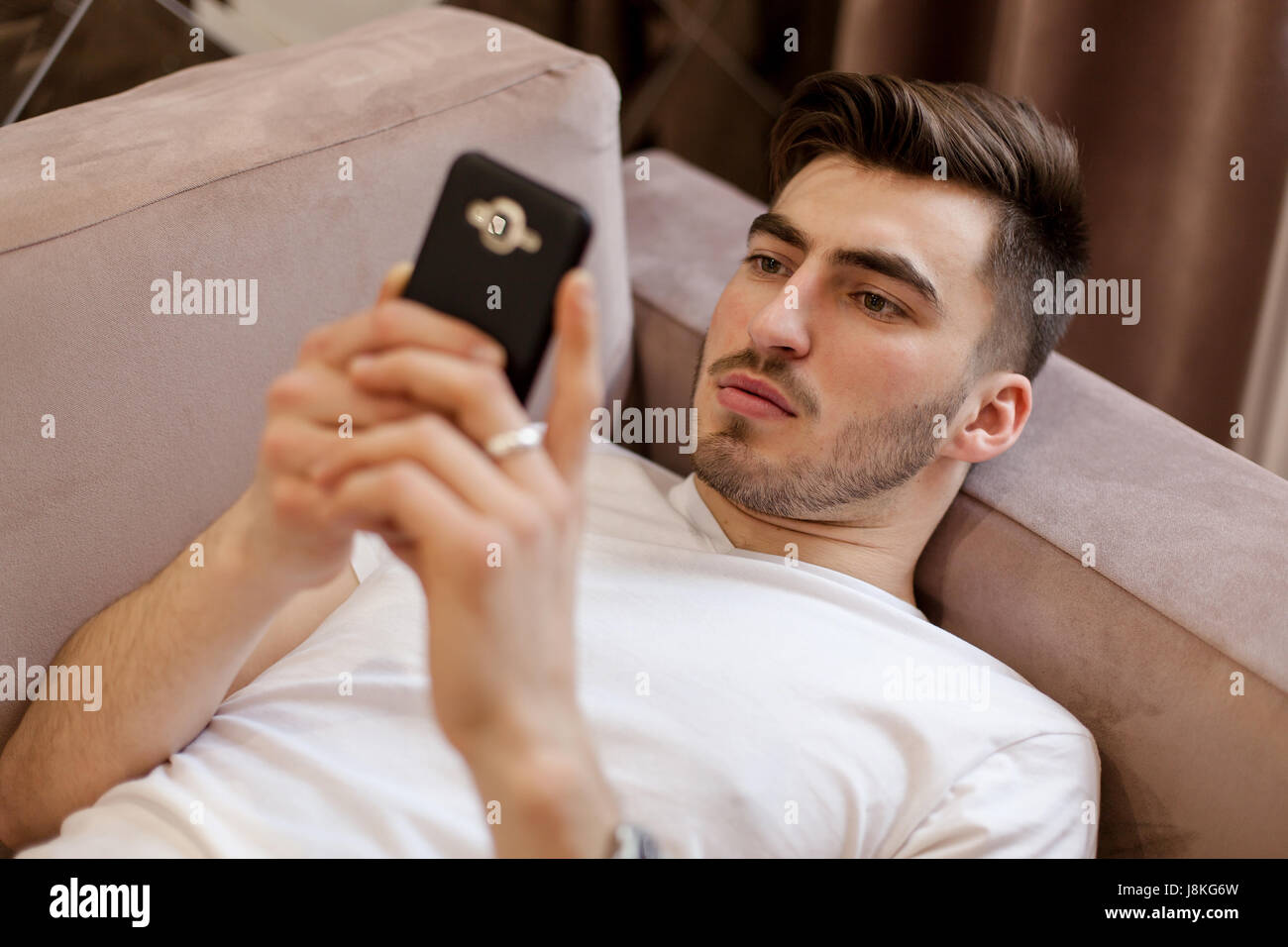 Hübscher junger Mann lag auf dem Sofa und Blick auf den Handy-Bildschirm. Stockfoto