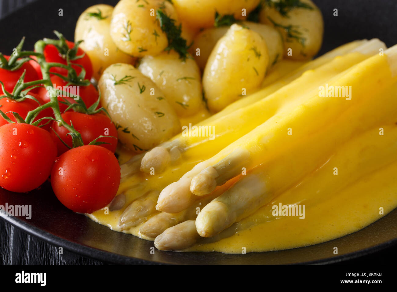 Essen Frühling: Spargel mit Sauce Hollandaise, Kartoffeln, Greens und Tomaten Nahaufnahme auf einer schwarzen Platte. horizontale Stockfoto