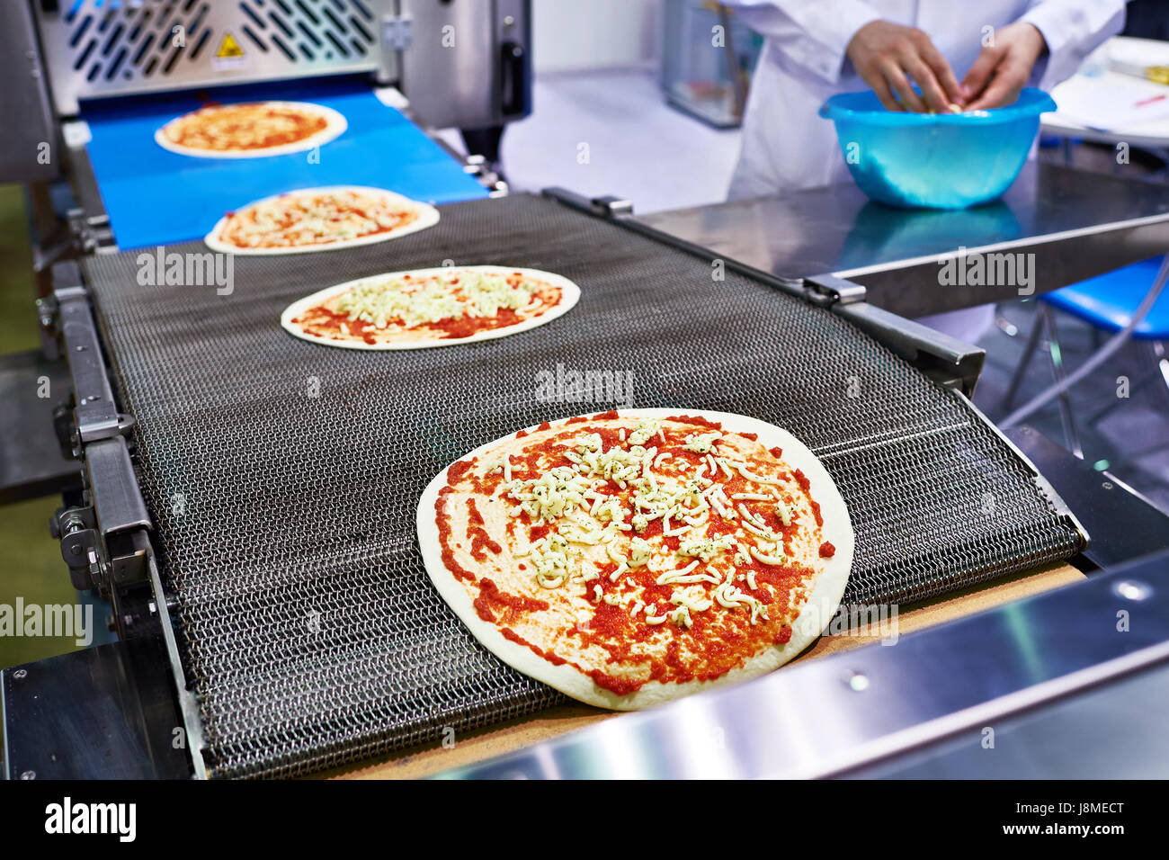 Arbeiter Bäcker Koch fügt Käse auf die Pizza auf dem Förderband Stockfoto