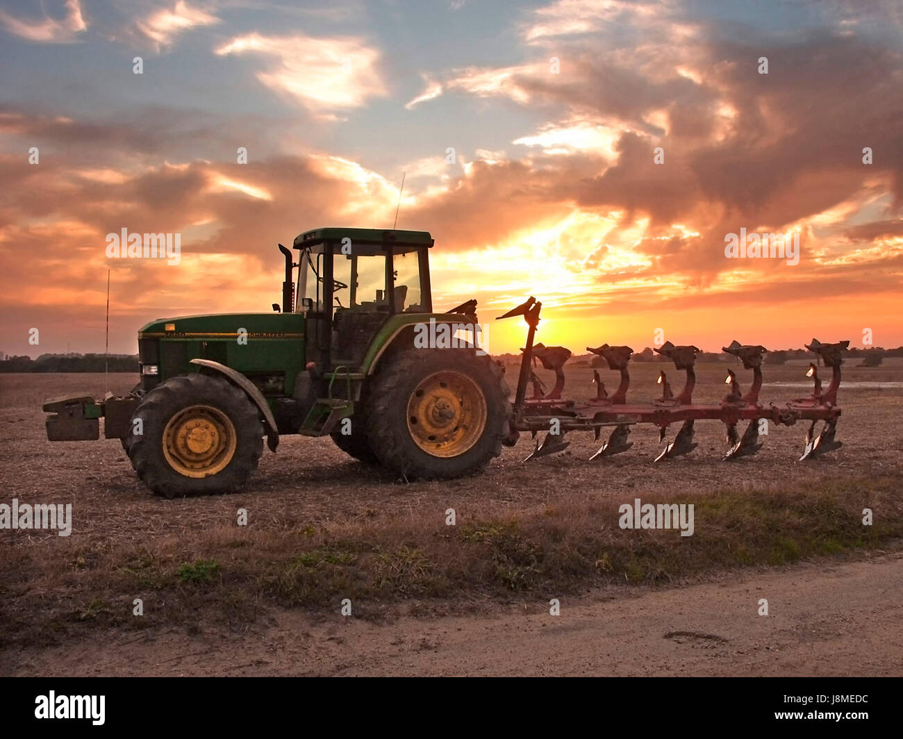 John Deere Traktor und vernetzter Pflug auf Ackerland geparkt mit echtem goldenen Himmel über dem Sonnenuntergang oder Sonnenaufgang, wenn Sie Essex England möchten Stockfoto